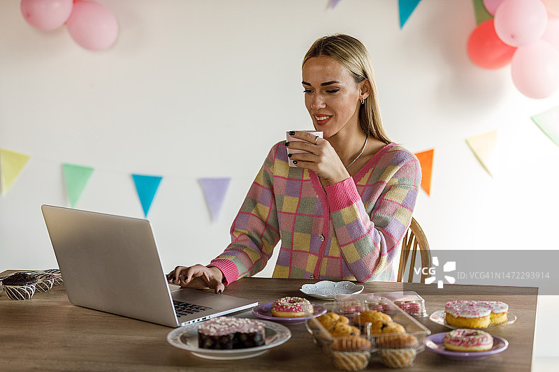 年轻女人计划派对甜点时，享受咖啡并使用笔记本电脑图片素材