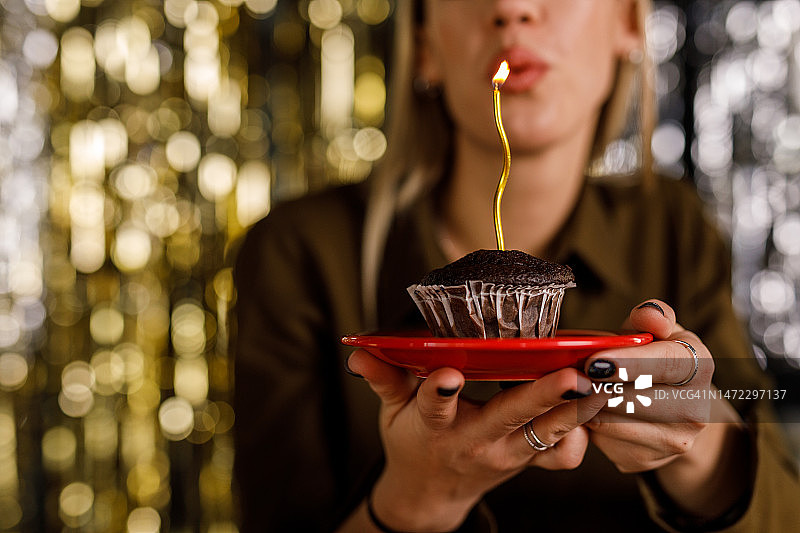 快乐的年轻女子吹灭巧克力松饼上的生日蜡烛图片素材
