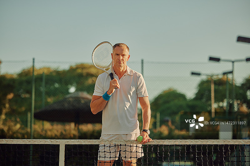 网球肖像：户外球场上表情严肃的年长男子和运动球网。老年运动员的运动球、锻炼和健身，背景模糊，准备锻炼和训练图片素材