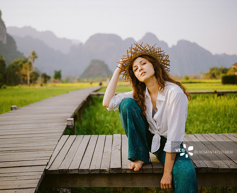 身穿白衬衫、头戴草帽漫步在稻田上的优雅女子图片素材