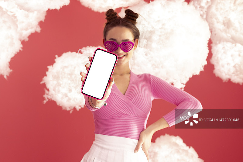 快乐的女孩穿着粉红色上衣和短裙，展示手机屏幕样机图片素材
