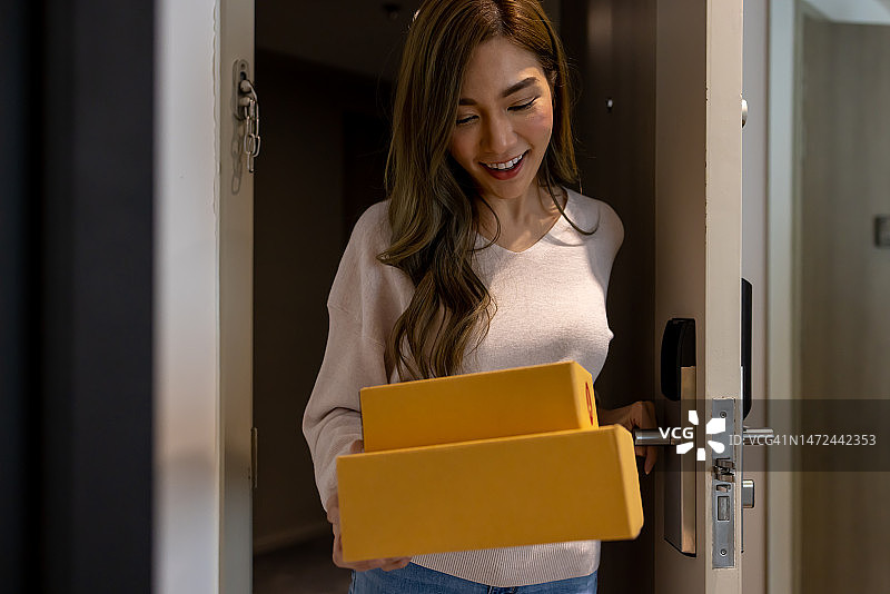 快乐的年轻亚洲女性在家门口抱着箱子图片素材
