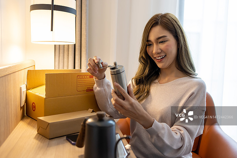 亚洲女性打开一个网上订购的手磨咖啡研磨器包裹，接收和拆包网上购买的概念图片素材