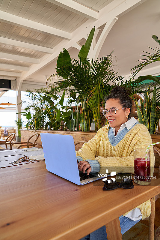 年轻的拉丁裔女人在海滩酒吧使用笔记本电脑工作图片素材
