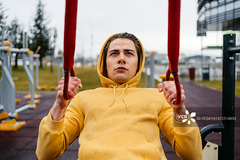 在雨中公园使用阻力带锻炼的年轻男人图片素材