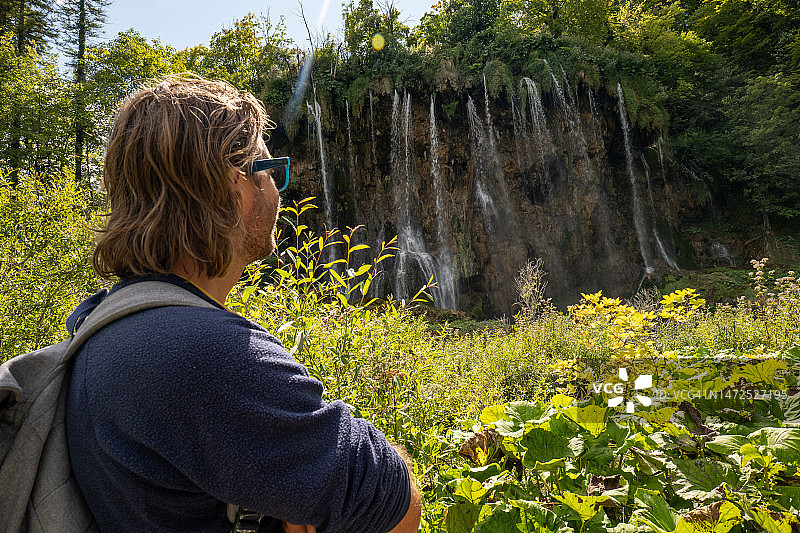 青年男人欣赏郁郁葱葱环境中的瀑布图片素材