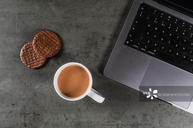 一杯茶和巧克力饼干，旁边是桌上的笔记本电脑图片素材