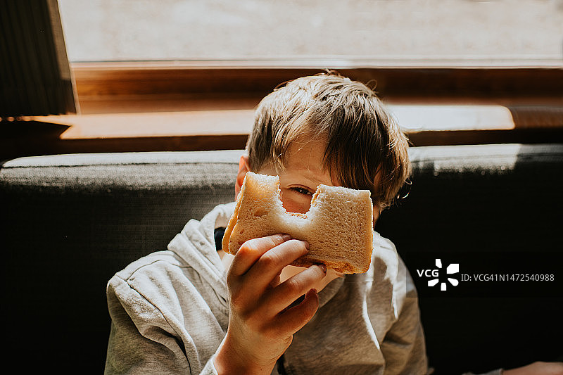 一个男孩顽皮地从他刚咬过的三明治的缺口中窥视。图片素材