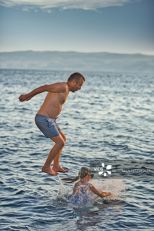 快乐的父女在地中海海滩度假，从码头跳入蓝色大海图片素材