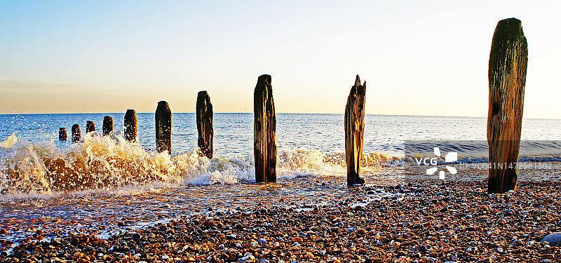 英国海浪冲刷旧木桩的圆石滩图片素材