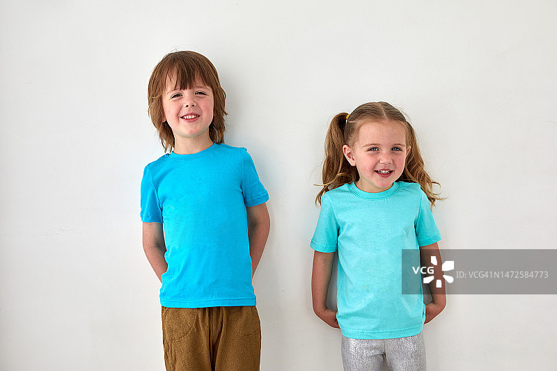 穿着蓝色T恤的可爱兄妹靠在灰色墙壁上图片素材
