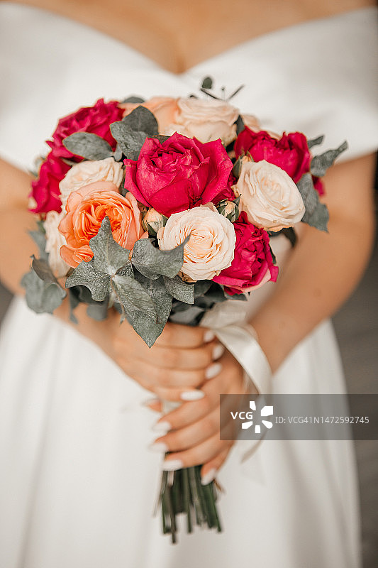 年轻新娘手捧粉橙色牡丹和玫瑰婚礼花束的腰部特写，俄罗斯图片素材