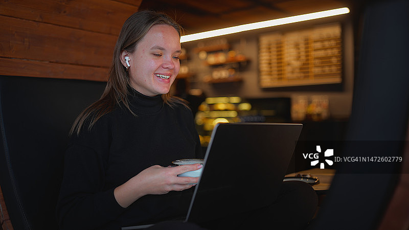 女人在咖啡馆舒适地坐着，一边享用热饮一边用笔记本电脑进行视频通话图片素材