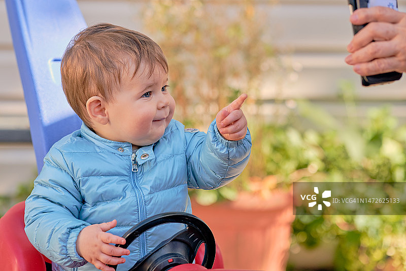 坐在玩具车里的幼儿通过手机上的视频会议与家人互动，美国纽约图片素材
