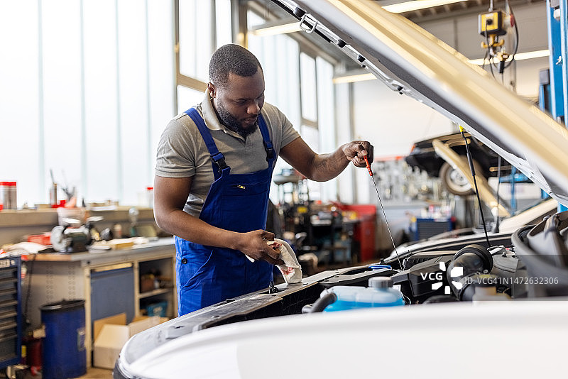 年轻技工在汽车服务站检查汽车发动机油位图片素材