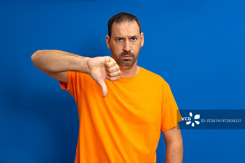 身穿橙色T恤的英俊男人，站在蓝色背景前图片素材