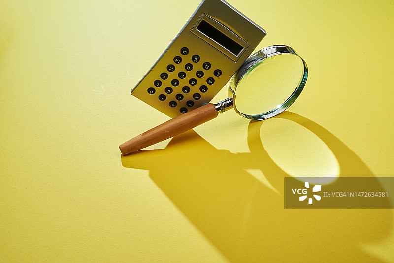 黄色背景下的计算器和放大镜，马来西亚图片素材