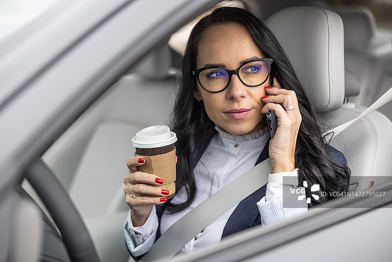 戴眼镜的女士在车内方向盘后拿着外卖咖啡杯听电话图片素材