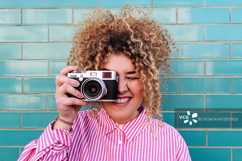手持复古相机的女人和蓝色砖墙背景图片素材