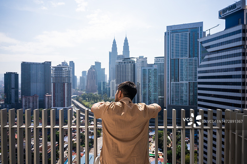 男人站在阳台上看着吉隆坡城市天际线图片素材