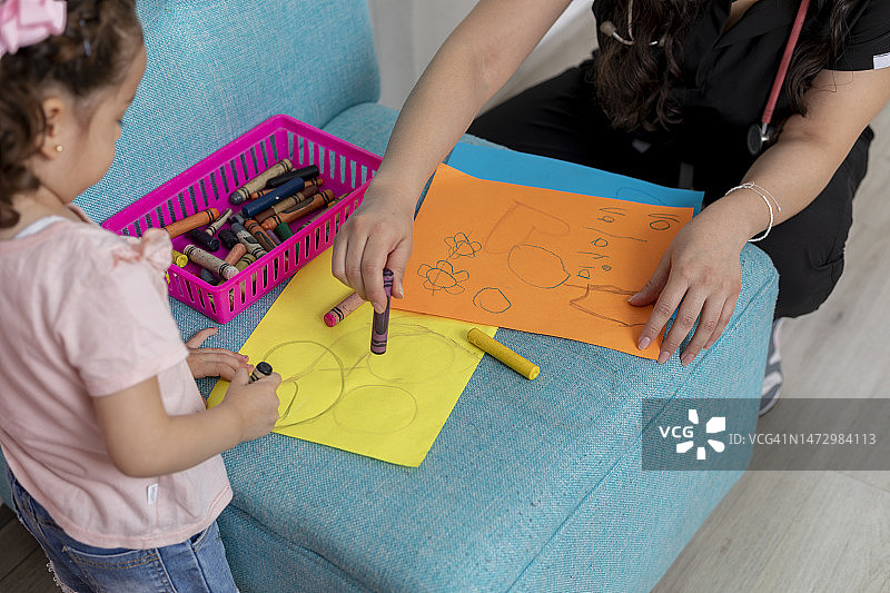 在医生办公室里，儿科医生监督下女孩在彩色纸上画画图片素材