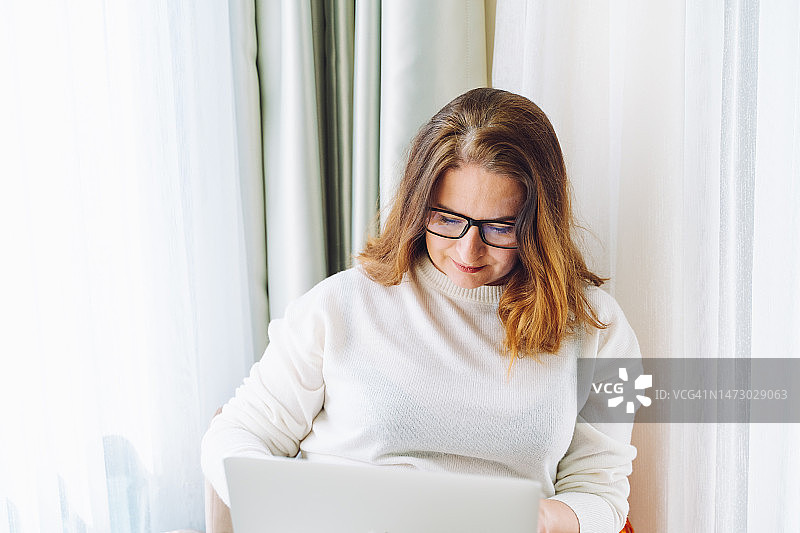 作家赶截止日期：女作家在明亮的窗边用白色笔记本电脑图片素材