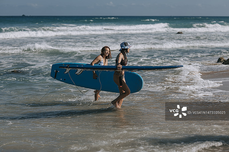 两名中国女性冲浪者 carrying 冲浪板归来图片素材