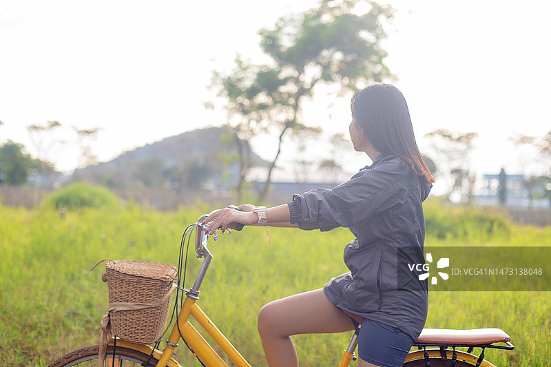 亚洲女孩在清晨的阳光下骑自行车看着草地图片素材