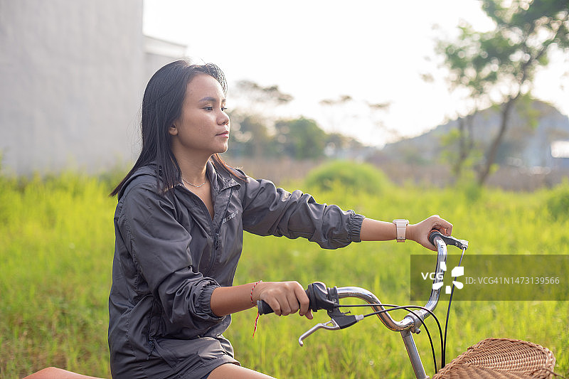 亚洲女孩在清晨的阳光下骑自行车看着草地图片素材