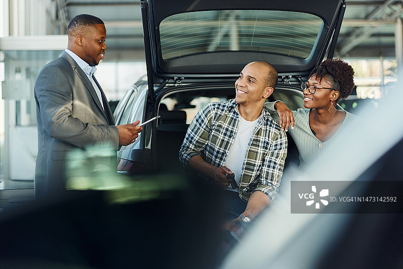 在展厅里与汽车销售员交谈的幸福情侣图片素材