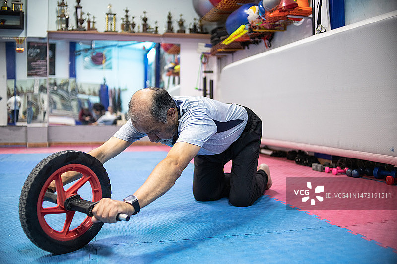 在健身房用腹部滚轮锻炼的老年男人图片素材