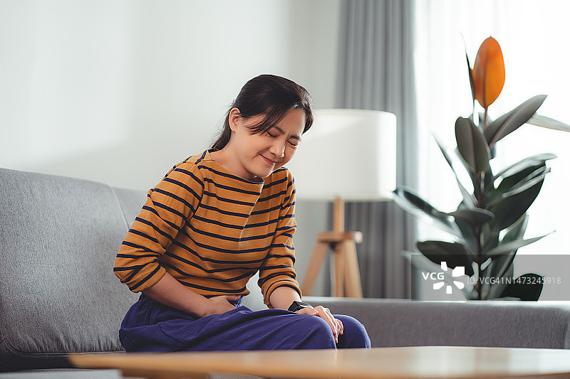 亚洲女人坐在客厅沙发上感到胃痛图片素材