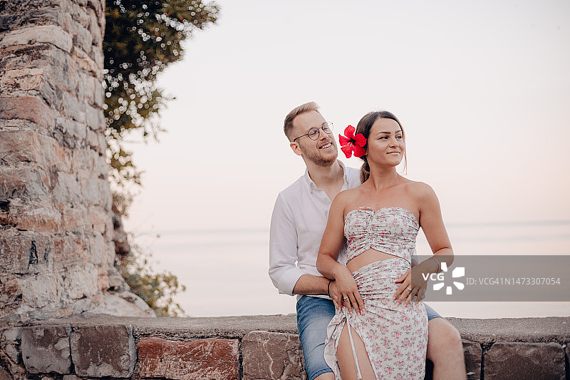 年轻情侣坐在海边岩石上眺望远方图片素材