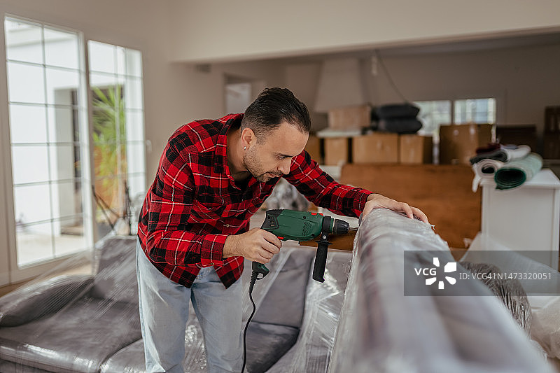 年轻男人用电动螺丝刀安装家具腿图片素材