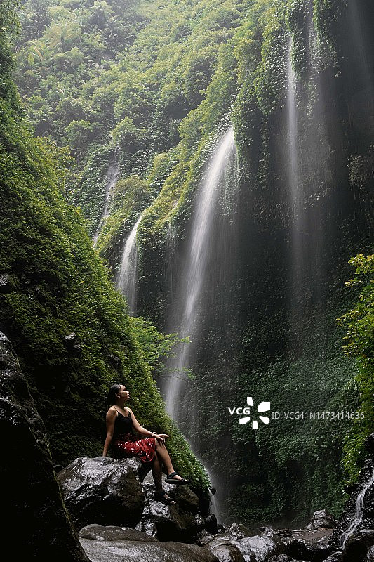 身穿红色蜡染布的东南亚女孩在瀑布下图片素材