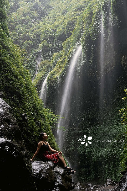 身穿红色蜡染布的东南亚女孩在瀑布下图片素材