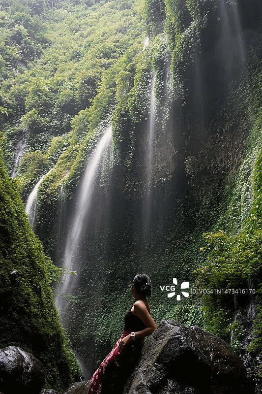 身穿红色蜡染布的东南亚女孩在瀑布下图片素材