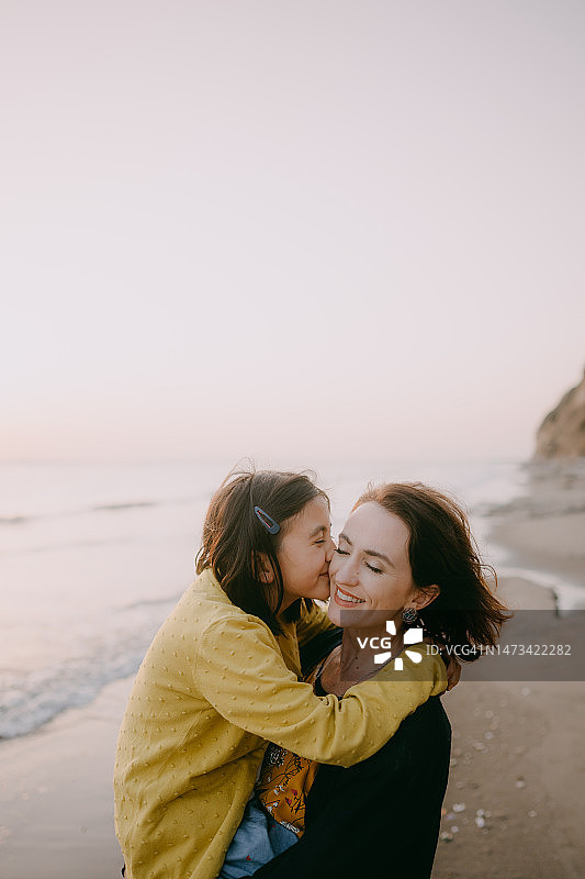 年轻女孩在日落时分在海滩上亲吻她的母亲图片素材