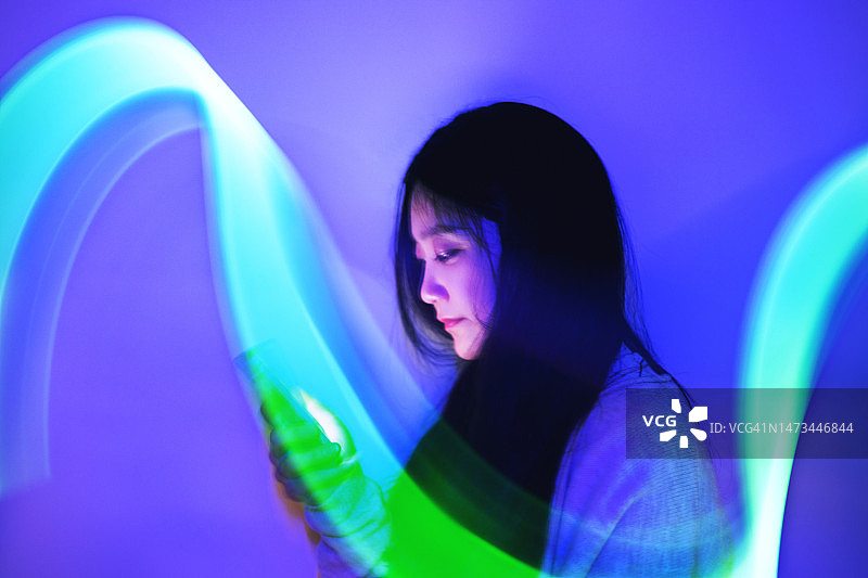 全息背景下年轻亚洲女性用智能手机图片素材