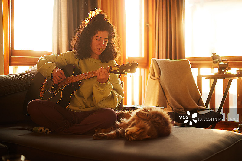 一位女士在家里的猫咪面前弹吉他图片素材