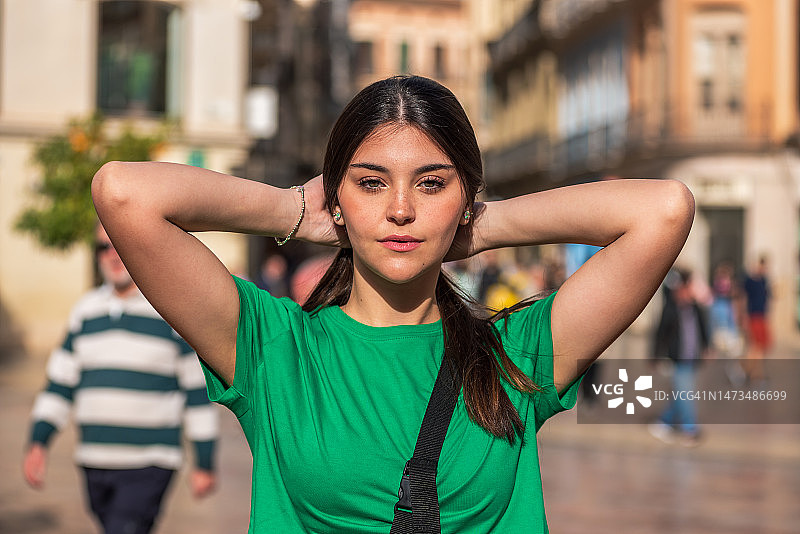 长发绿衣少女在人群中触摸头发，肩挎包漫步城市街头图片素材