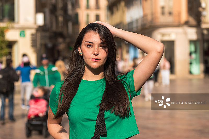 长发绿衣少女在人群中触摸头发，肩挎包漫步城市街头图片素材