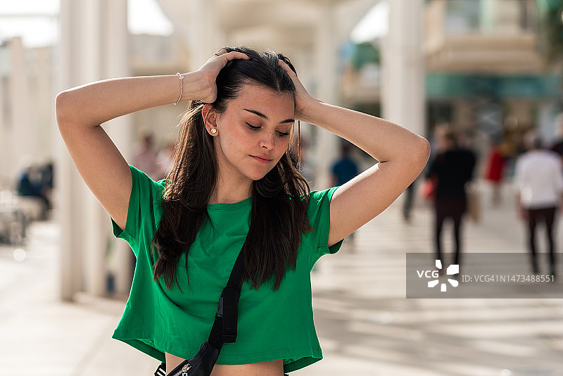 长发年轻女孩穿着绿色T恤走在人群中，抚摸着头发图片素材