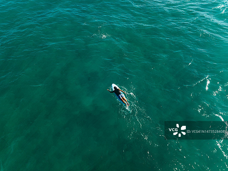 从空中视角看，在蓝色海洋中带着冲浪板的男冲浪者图片素材