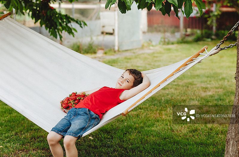 男孩躺在吊床上，手里拿着一杯草莓图片素材