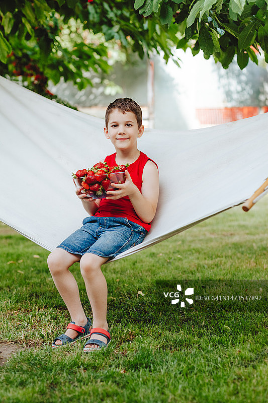 男孩躺在吊床上，手里拿着一杯草莓图片素材