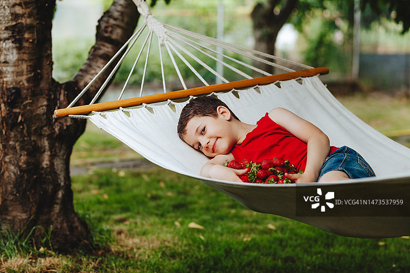 男孩躺在吊床上，手里拿着一杯草莓图片素材