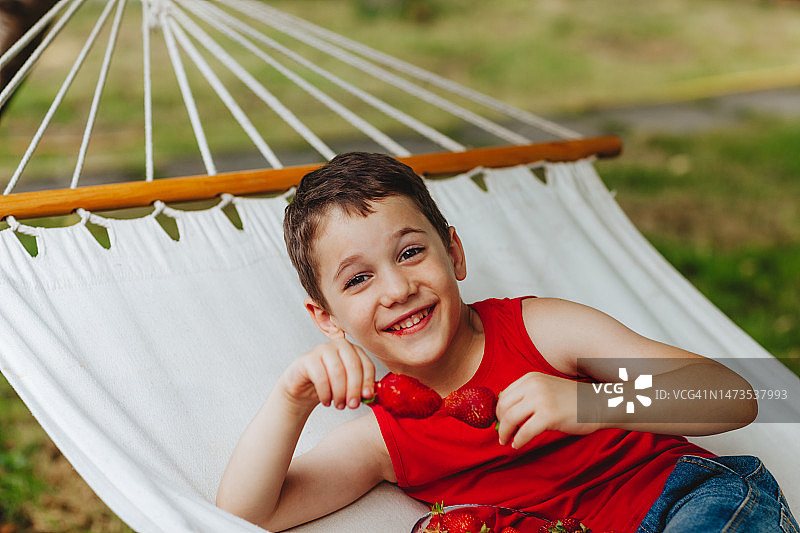 男孩躺在吊床上，手里拿着一杯草莓图片素材