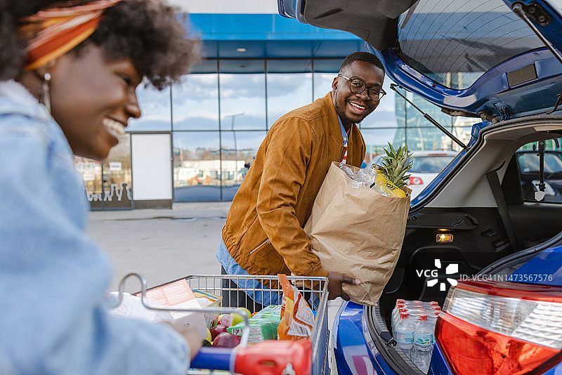 快乐的年轻夫妇在停车场将食品杂货放入汽车图片素材