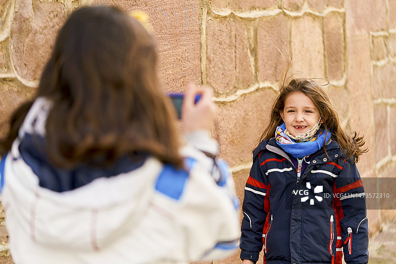女孩用手机给另一个女孩拍照的背影图片素材